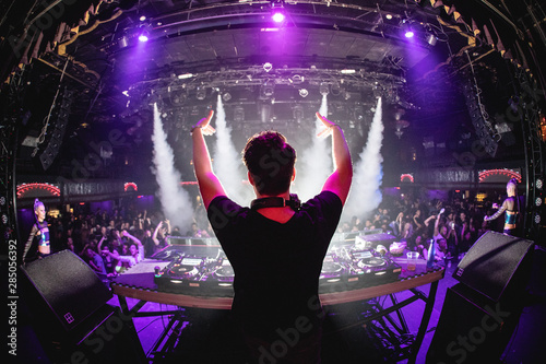 DJ in nightclub with hands up and cryo canons, shot from behind