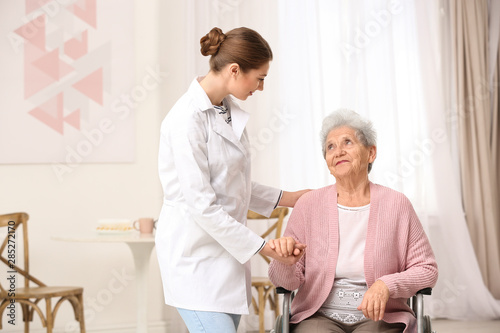 Nurse assisting elderly woman in wheelchair indoors