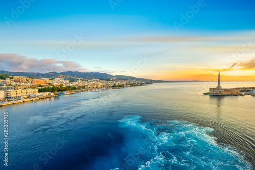 Sunrise from a cruise ship at the port of Messina, Italy on the island of Sicily in the Mediterranean Sea with the Golden Madonna della Lettera column in view