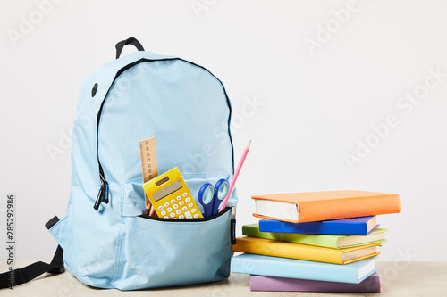 blue backpack with school supplies near books isolated on white