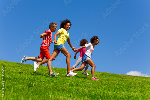 Four happy diverse looking children run on lawn