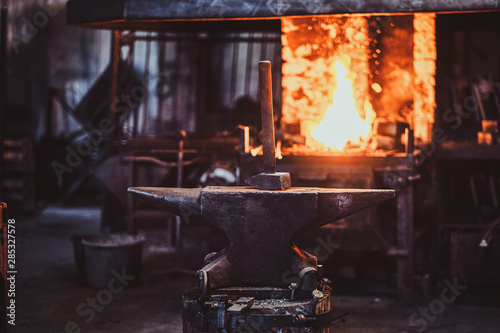 Hammer on anvil at dark blacksmith workshop with fire in stove at background.