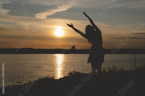 Silhouette of young dancing woman in sunset rays on a lake shore.