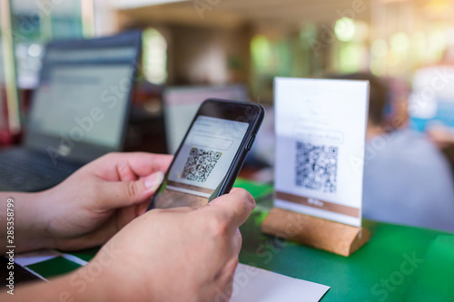 Closeup of a hand holding phone and scanning QR code with blurry cashier at counter service. Man hands paying with QR code. Customer hands making payment through smart phone and scan code.