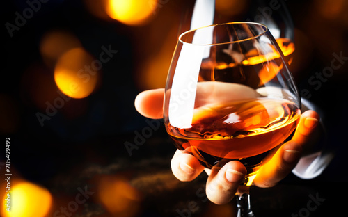 French glowing cognac glass in hand on the dark bar counter background, copy space, selective focus