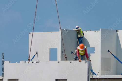 Construction worker are installing the precast concrete wall, orange safety helmet and green vest.