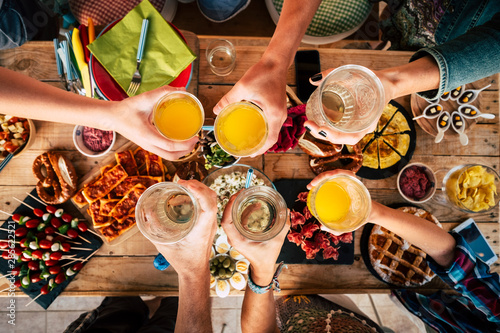 Group of friend mixed ages generations from children to adult have fun togeter with food and drinks - aerial top view of table and people toasting together in friendship - home or restaurant concept