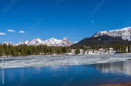 Molas Lake with melting ice, trees and snow-dappled mountains in Colorado