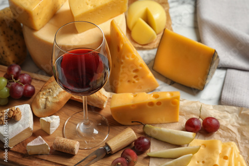 Board with different kinds of delicious cheese, snacks and wine on marble table