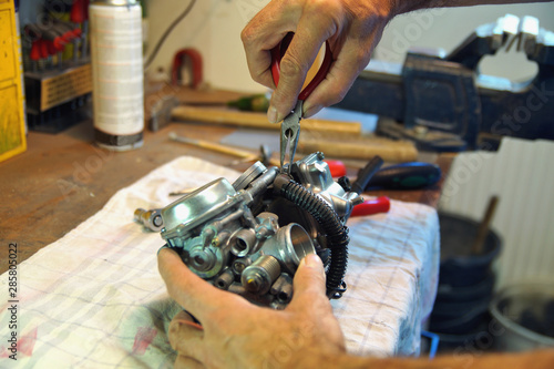 motorcycle carburetor. Automotive Carburetor Repair. Male Using A tong To Rebuild A Carburetor On A Workbench. Mechanic man checking carburetor of motorcycle. Repair. Maintenance and fixing concept. 