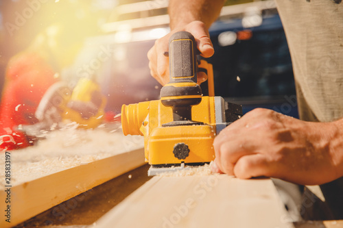 Male hands worker hold electric work planer with wooden board, smooth dust