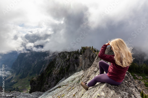 Adventurous Girl on top of a rugged rocky mountain during a cloudy summer morning. Taken on Crown Mountain, North Vancouver, BC, Canada.