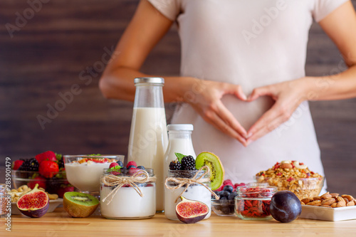 Female make shape of heart with her hands. Light summer breakfast with organic yogurts, fruits, berries and nuts. Nutrition that promotes good digestion and functioning of gastrointestinal tract.