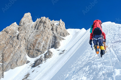 Climber reaches the summit of mountain peak enjoying the landscape view.
