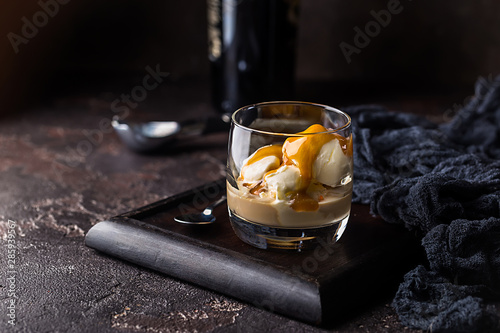 Ice cream with caramel topping and Irish cream liqueur in a glass over dark background.
