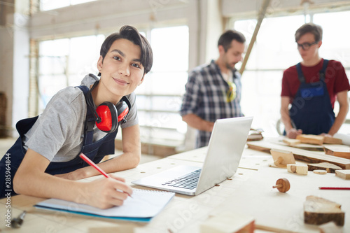 Portrait of modern carpenters working at woodworking factory, focus on young woman smiling at camera in foreground, copy space