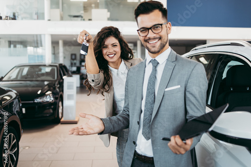 Happy and beautiful middle age business woman buying new car at showroom. A nice seller helps her make the right decision.