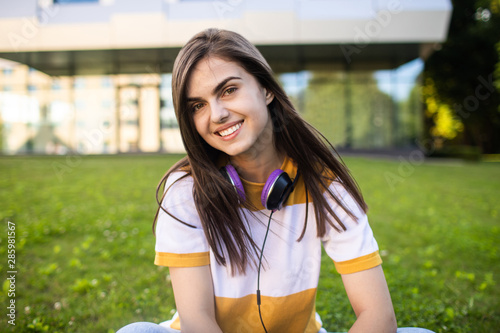 Portrait of smiling cute college girl with headphones posing in front of her alma mater