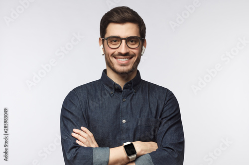 Portrait of smiling handsome man in denim shirt and smart watches, standing with crossed arms isolated on gray