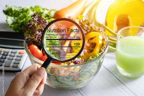 nutritional information concept. hand use the magnifying glass to zoom in to see the details of the nutrition facts from food , salad bowl