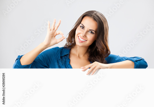 beautiful young businesswoman showing blank sign board with empty copy space place for some slogan or advertising text message, isolated over grey color background