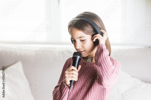 Niña cantando feliz con auriculares y micrófono en interior de casa