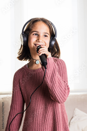 Niña cantando feliz con auriculares y micrófono en interior de casa