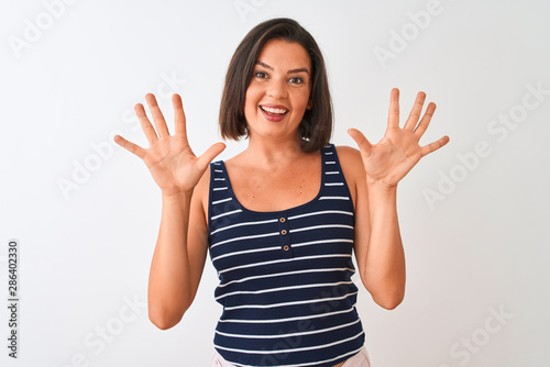 Young beautiful woman wearing blue striped t-shirt standing over isolated white background showing and pointing up with fingers number ten while smiling confident and happy.