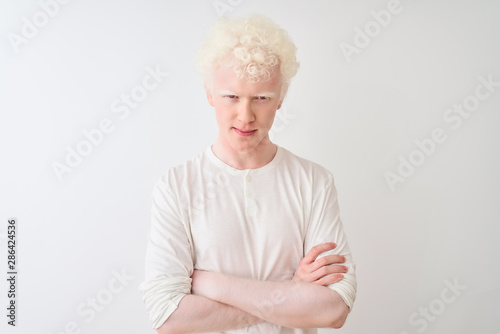 Young albino blond man wearing casual t-shirt standing over isolated white background skeptic and nervous, disapproving expression on face with crossed arms. Negative person.