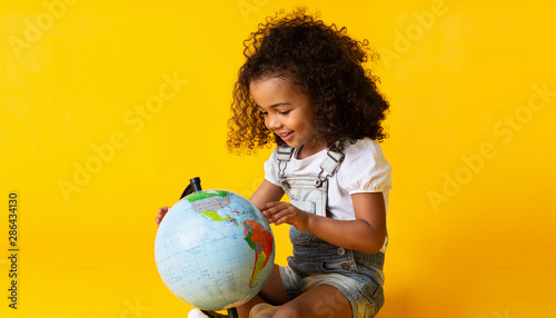 Cute little girl looking at earth globe, yellow background