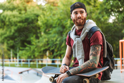 Attractive cheerful young man sitting at the skate park ramp