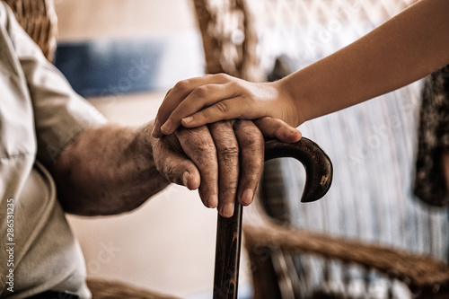 child's hand over old man's hand holding a cane.