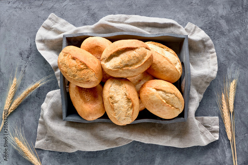 Bread buns in basket on rustic wood with wheat ears, top view on