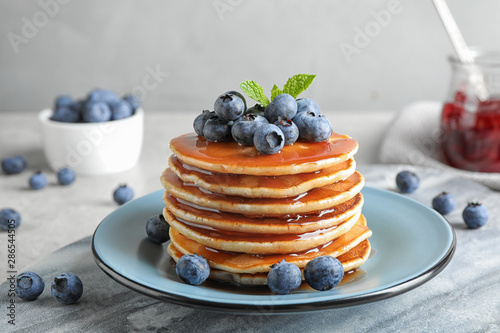 Plate of delicious pancakes with fresh blueberries and syrup on grey table against light background