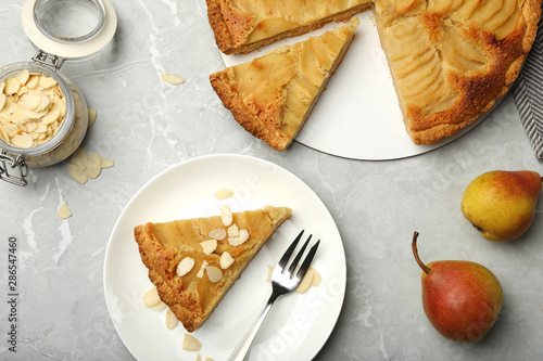 Cut delicious sweet pear tart and almond flakes on grey marble table, flat lay