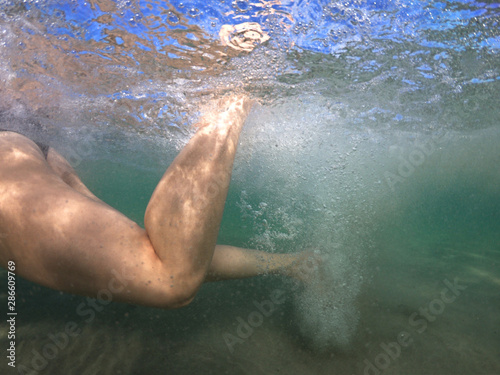 Unidentified woman's feet underwater swimming with effort and releasing air bubbles to reach the shore