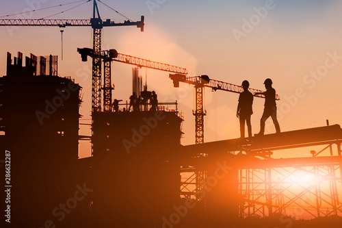 Silhouette Two engineers consult and inspect high-rise construction work over blurred industry background with Light fair.Create from multiple reference images together