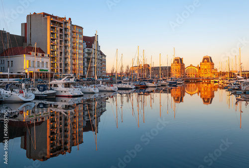 Reflection of the yacht sailing ships and Ostend (Oostende in Flemish) city train station in the harbor at sunset, Ostend, Belgium.