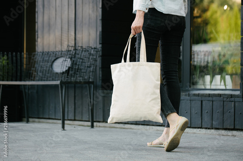 Woman holding white textile eco bag against urban city background. . Ecology or environment protection concept. White eco bag for mock up.