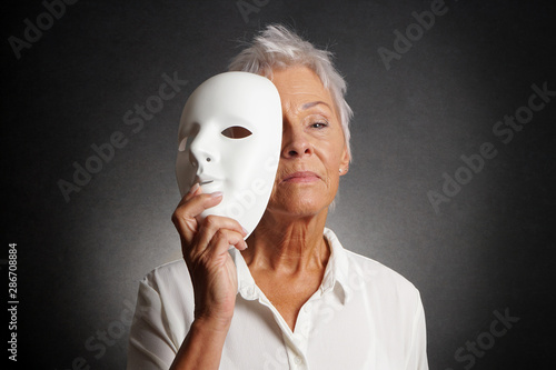 serious looking older woman revealing true face behind mask
