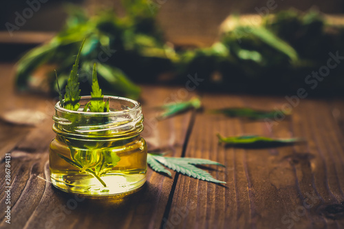 Glass jar with hemp oil and fresh leaves on wooden background