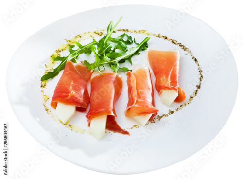 Tasty dish rolls of prosciutto di parma with melon served with arugula at plate