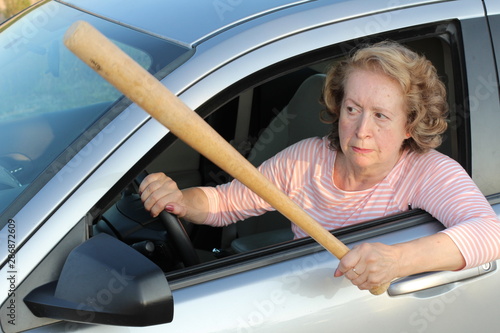 Angry mature female driver holding baseball bat 