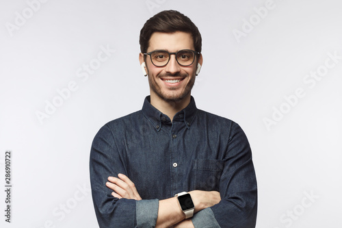 Smiling handsome man in denim shirt and smartwatch, standing with crossed arms isolated on gray background