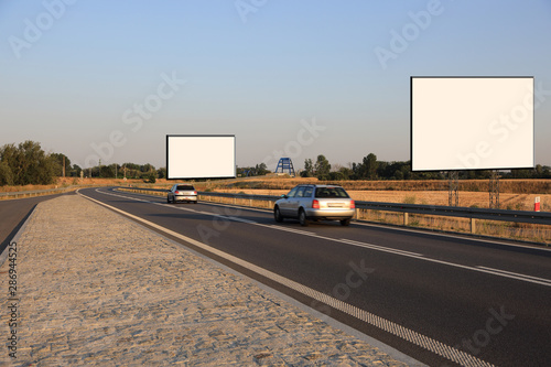 Puste bilbordy reklamowe przy drodze szybkiego ruchu o zachodzie słońca, samochody osobowe.