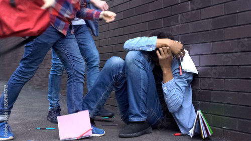 Cruel teenagers scattering classbooks of afro-american boy, school bullying