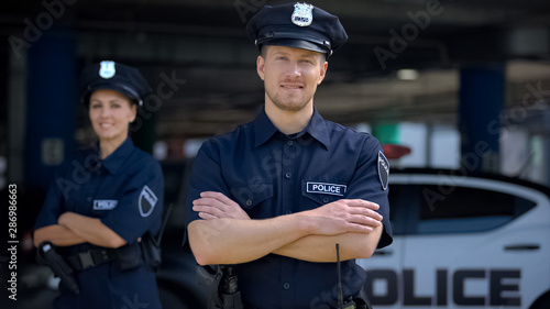 Kind police officers smiling standing near police station, ready to help, order