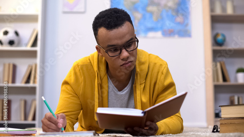 Afro-american student writing essay, preparing for important lectures in college