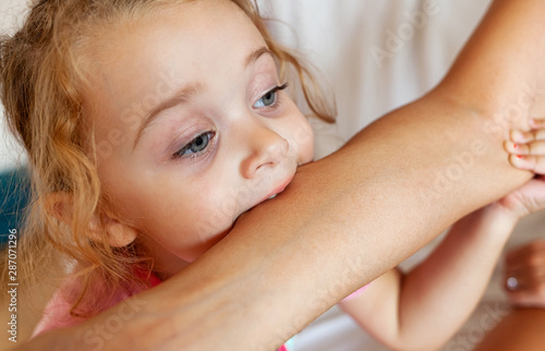 Toddler female biting the arm of the mother.