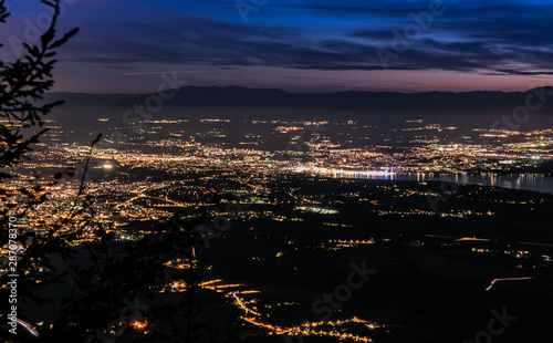 Evening top view of city lights, French Annemasse, Swiss Geneva,lake Geneva and picturesque sky with dark clouds after sunset,photo with long exposure.Department of Haute-Savoie in France.